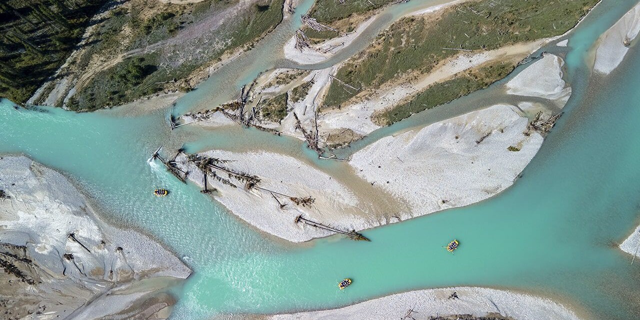 Aerial view of the Kicking Horse River, showcasing its turquoise waters, winding channels, and whitewater rafters navigating through the stunning landscape.