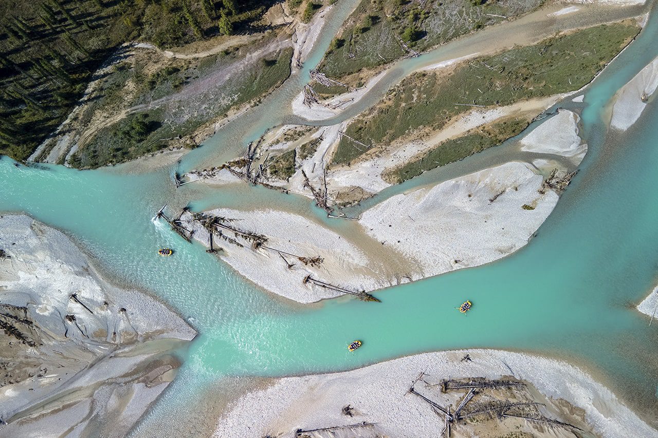 Aerial view of the Kicking Horse River, showcasing its turquoise waters, winding channels, and whitewater rafters navigating through the stunning landscape.