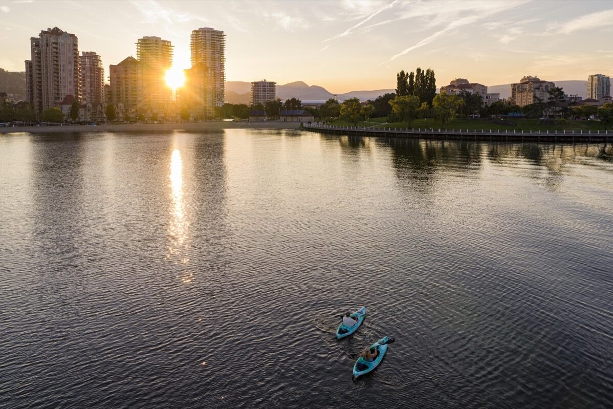 Aerial view of kayakers paddling through downtown Kelowna, surrounded by city skyline and waterfront scenery.
