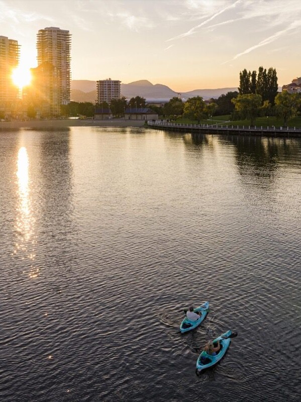 Aerial view of kayakers paddling through downtown Kelowna, surrounded by city skyline and waterfront scenery.