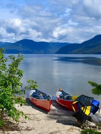 Two canoes resting on the sandy shore of Murtle Lake, British Columbia, with majestic mountains as a backdrop.