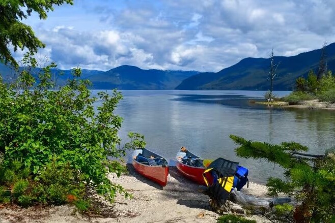 Two canoes resting on the sandy shore of Murtle Lake, British Columbia, with majestic mountains as a backdrop.
